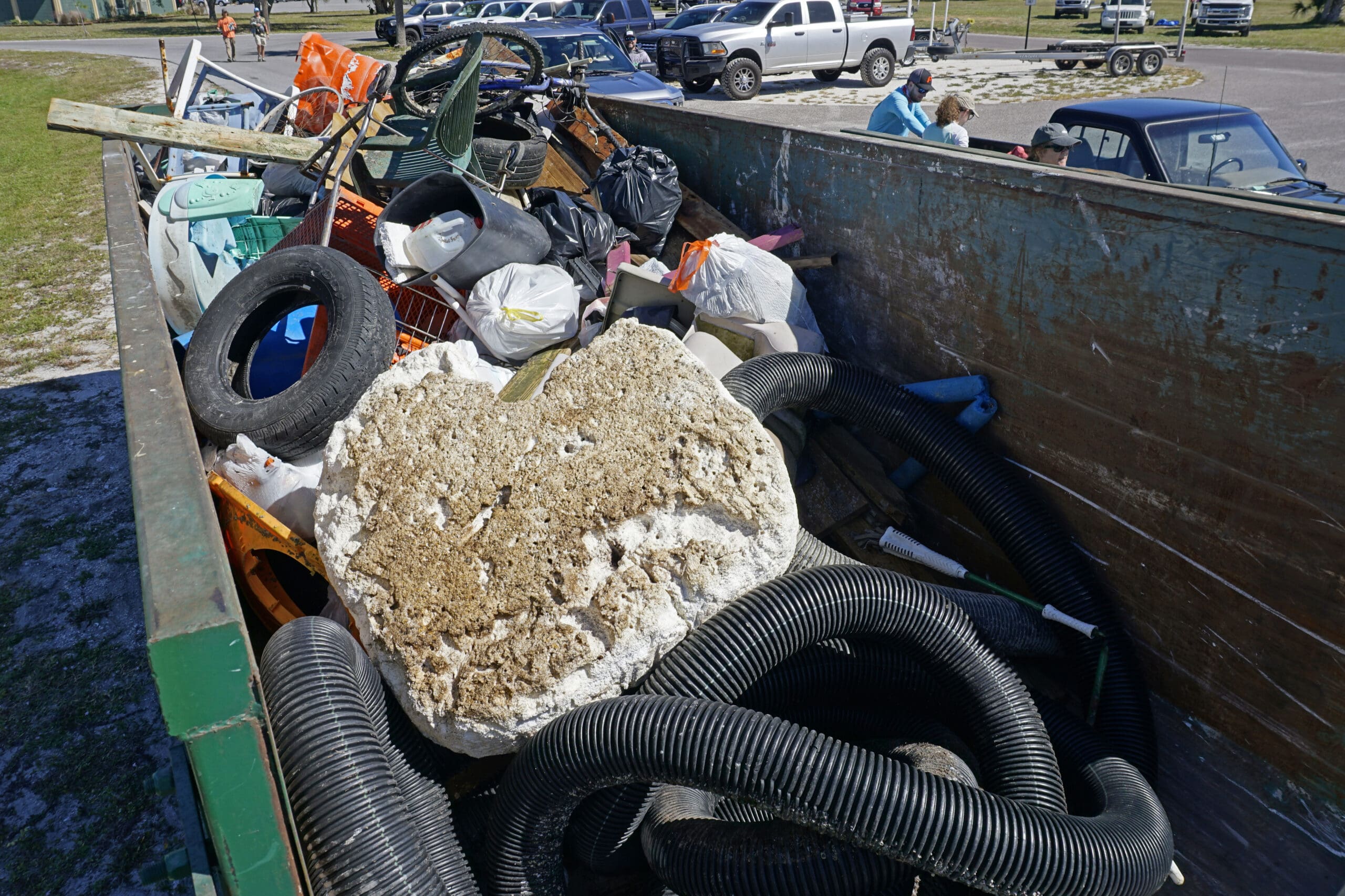 A dumpster filled with trash, including a tire and barnacle covered buoy.