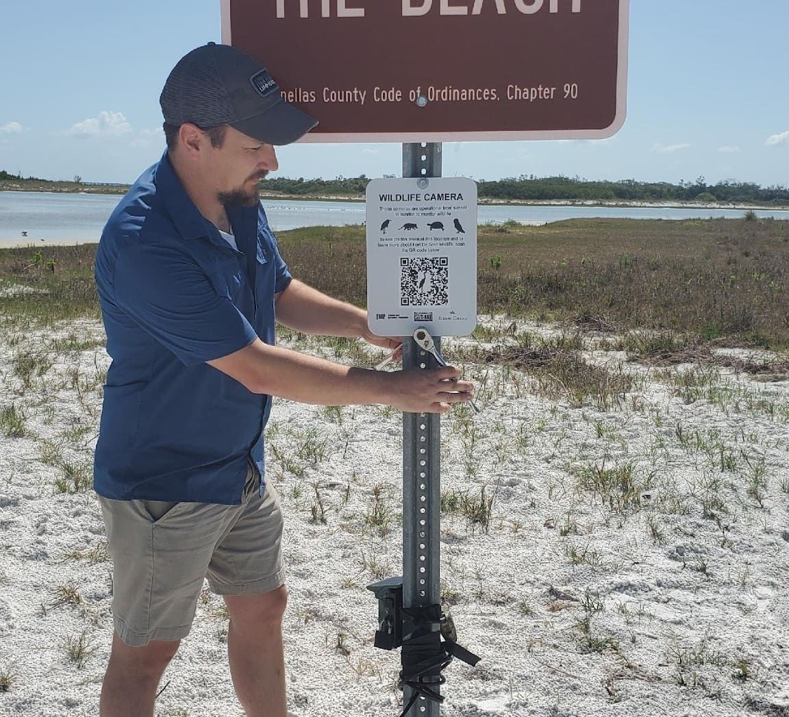 man using tools to install a sign on a post at the beach